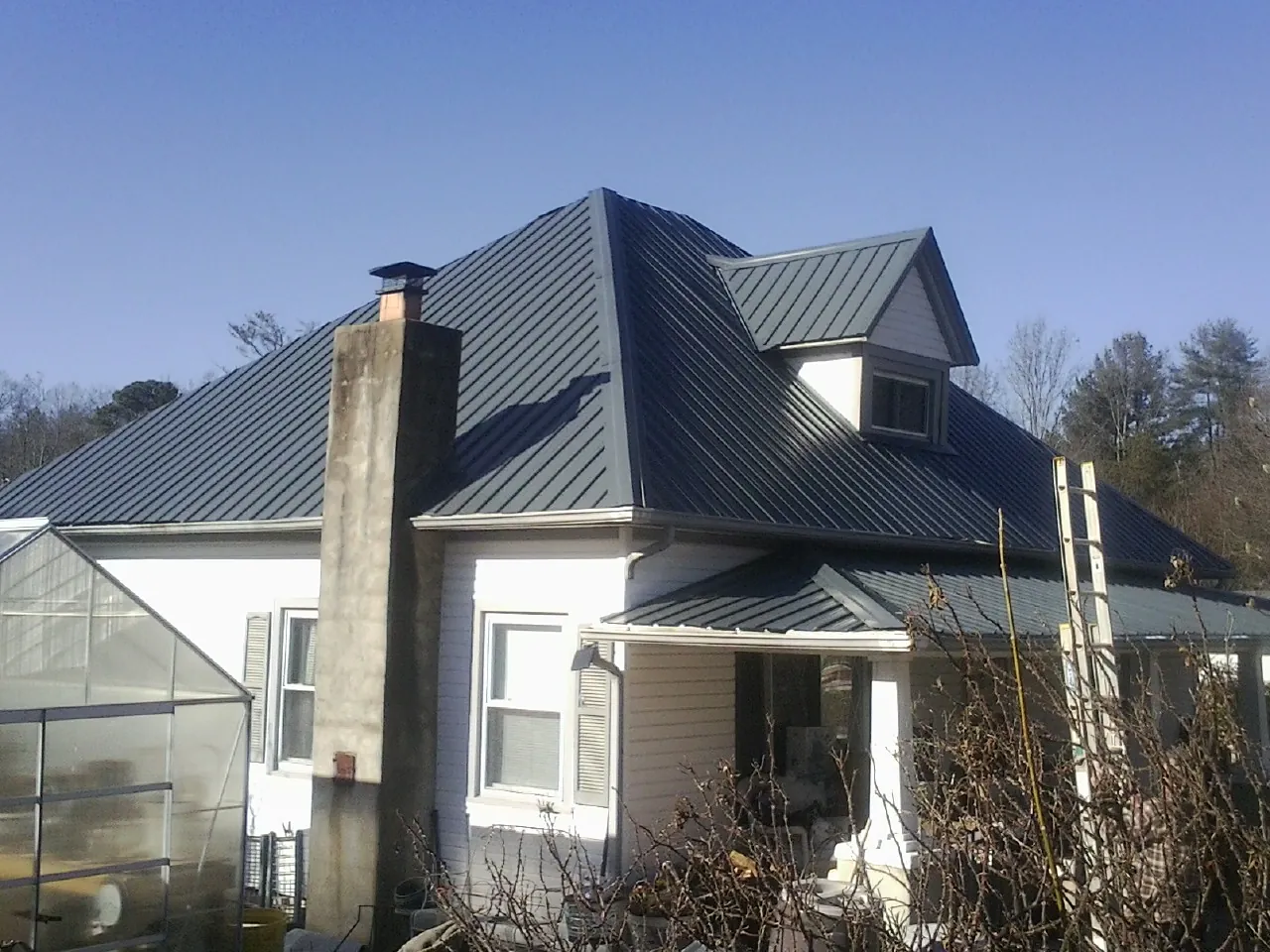 Dark blue standing seam metal roof on a white farmhouse with dormer — Slate & Tile Roof Repair by Roofing Brothers in Gay