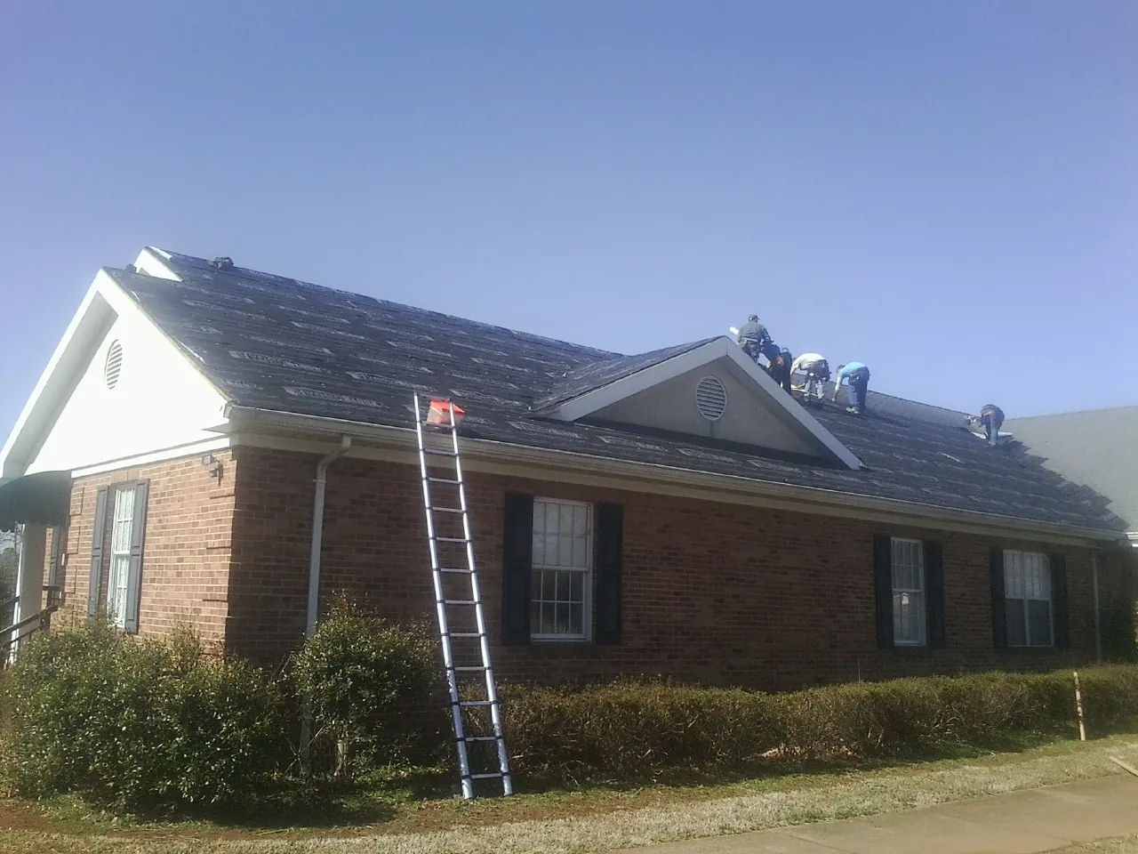 Crew tearing shingles off a brick ranch roof with a ladder set — Metal Roof Repair work by our crew in Gay