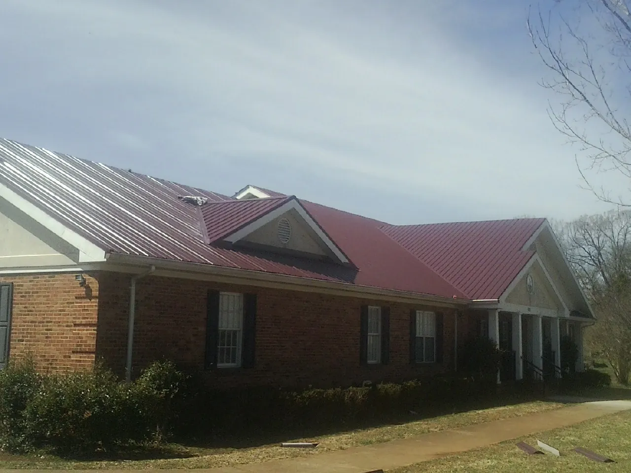 Red metal roof with gabled entries on a long brick building, from a Hail Damage Roof Repair job in Gay