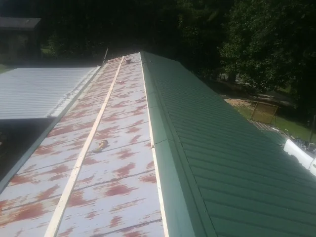 Old rusted panels beside newly installed green metal roofing — Wind Damage Roof Repair by Roofing Brothers in Gay