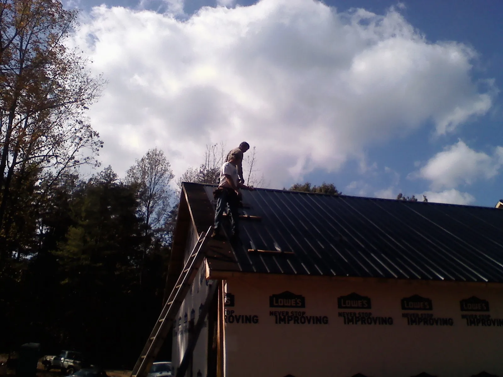 Roofer fastening dark metal panels high against a cloudy sky, from a Roof Inspection job in Gay