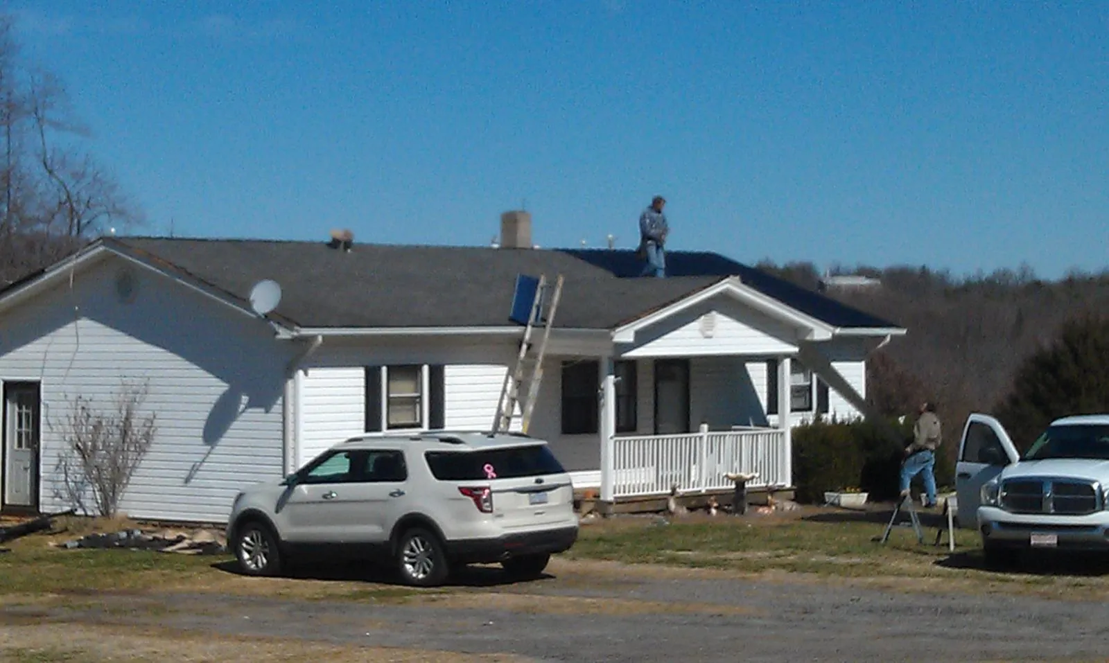 Roofers stripping shingles from a white ranch house roof in Gay