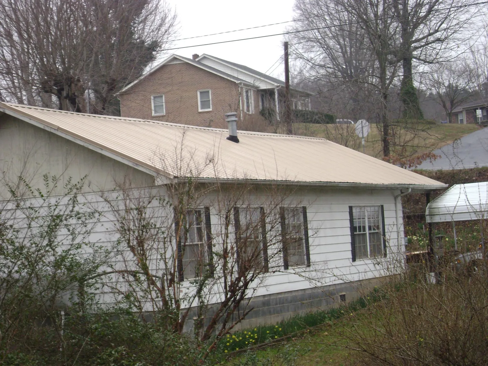 Tan metal roof on a white sided house set into a hillside — Commercial Roofing by Roofing Brothers in Gay