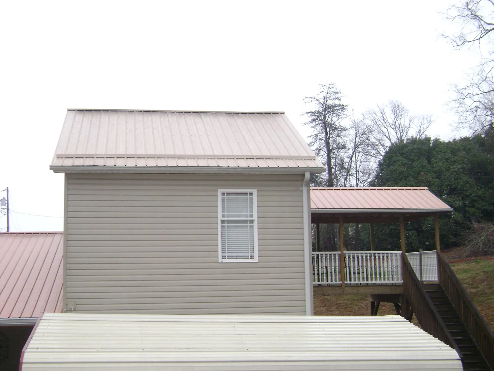 Tan metal roofs on a two story addition and attached porch, from a Roof Replacement job in Gay
